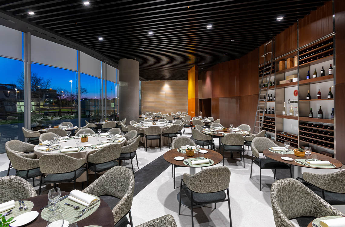 Elegante restaurante del hotel Alexandre Corporativa con mesas puestas y una moderna bodega de vinos.