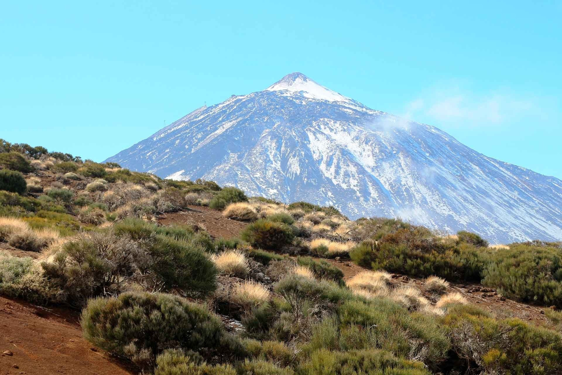 Alexandre Corporativa: Sommet enneigé, paysage volcanique aride sous ciel bleu.