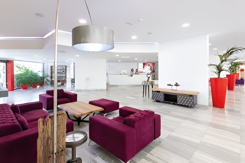 Modernes Lobby-Design des Alexandre Corporativa Hotels mit lila Sofas, Pflanzen und Rezeption.