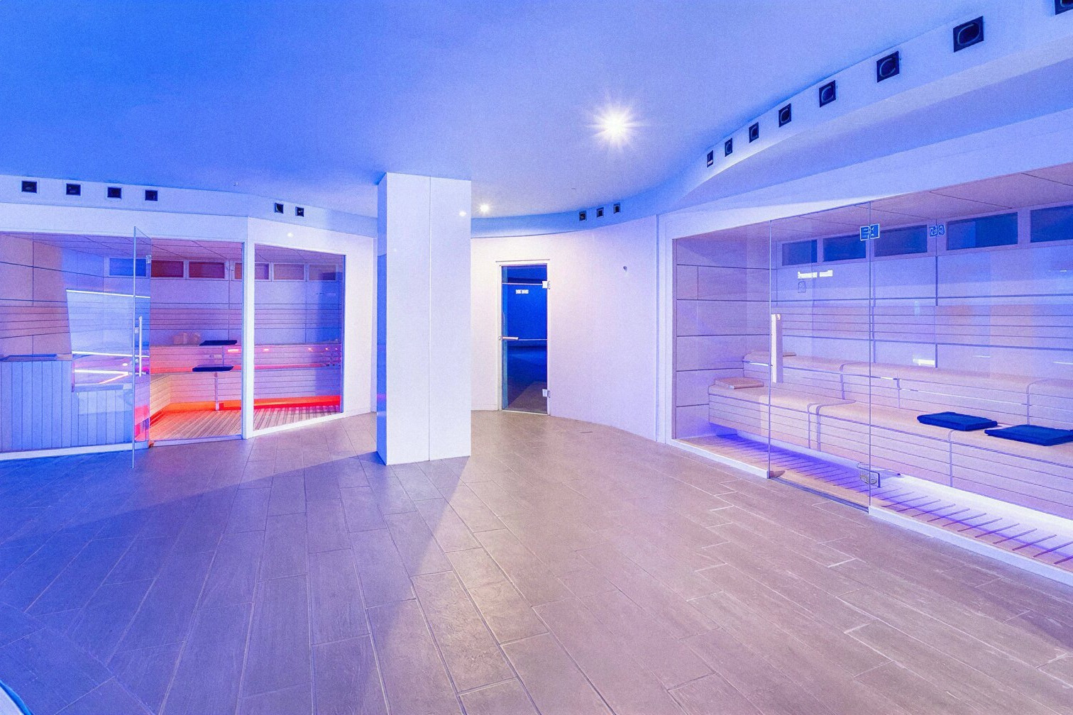Spa moderno de Alexandre Corporativa con saunas de cromoterapia rojas y azules y luz ambiental LED.