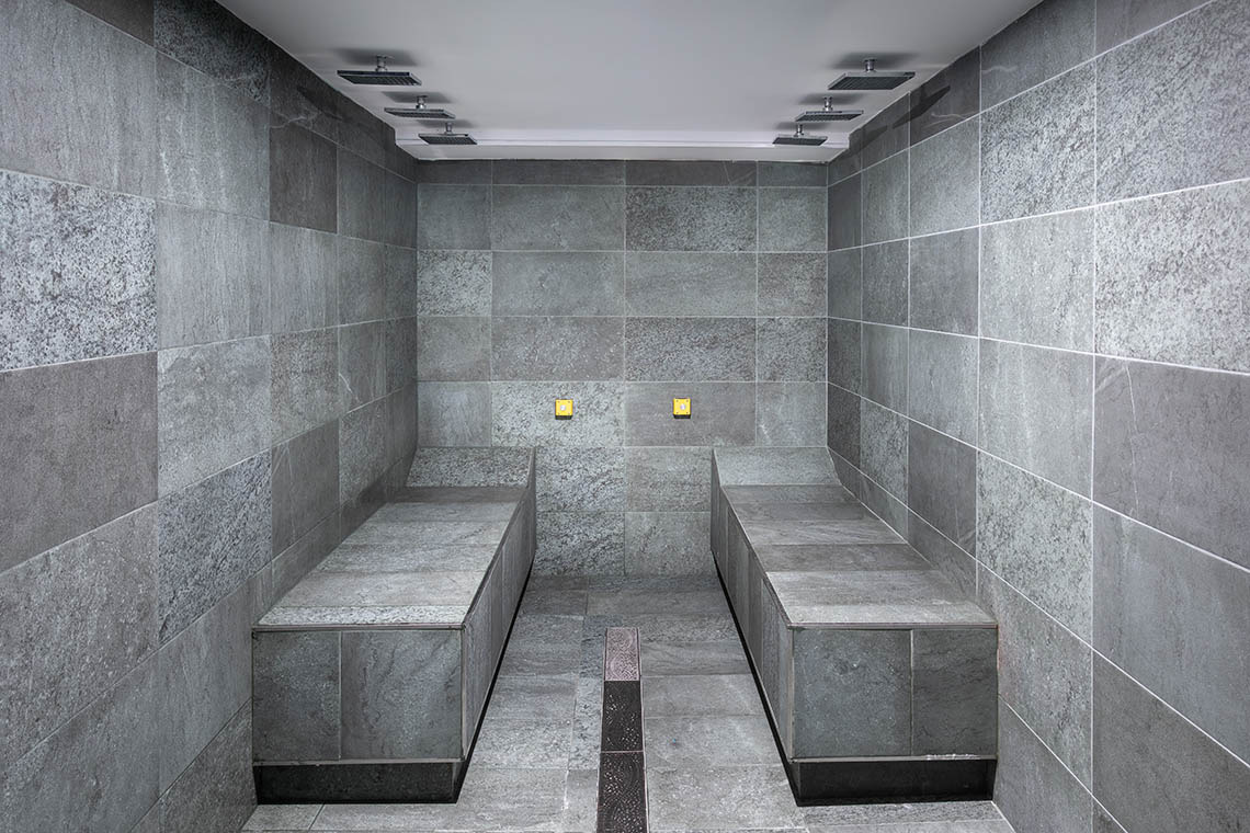 Ducha Alexandre Corporativa: Salas de vapor con bancas de piedra y duchas de lluvia.