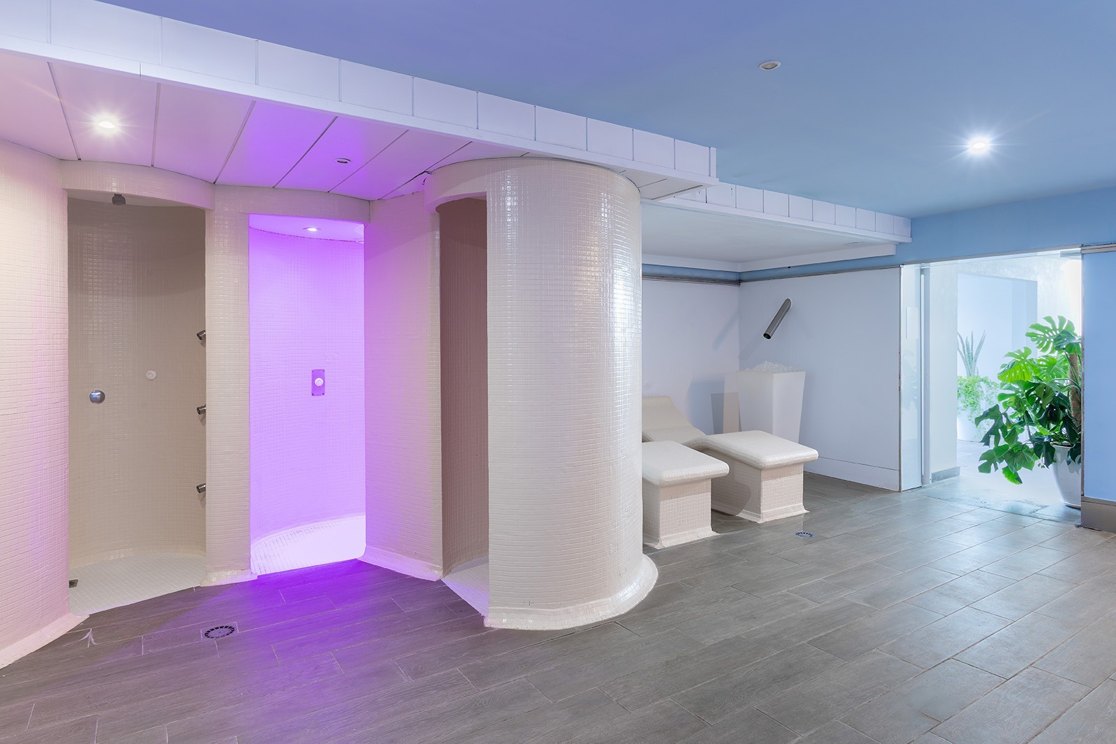 Moderna zona de spa del hotel Alexandre Corporativa con duchas, bancos de relajación y luz morada.