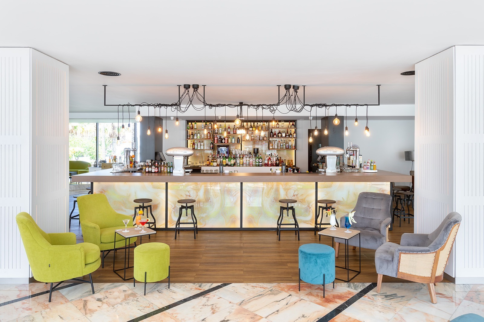 Moderno bar de hotel en Alexandre Corporativa con asientos vibrantes, cócteles y luces elegantes.