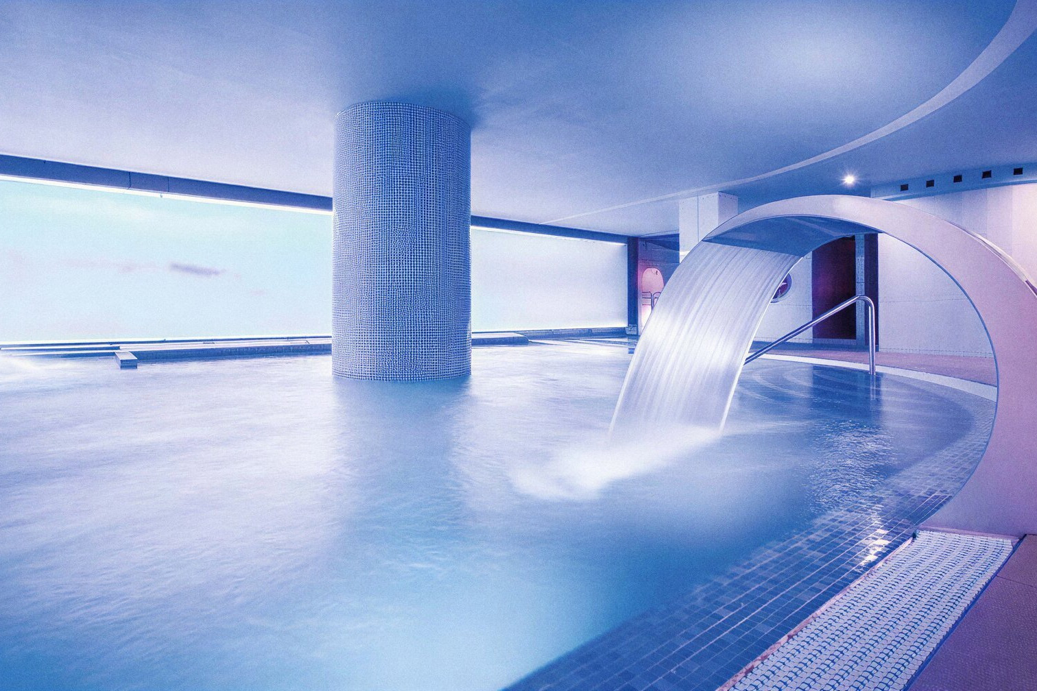 Piscina climatizada con cascada en el spa de Alexandre Corporativa, un oasis de tranquilidad.