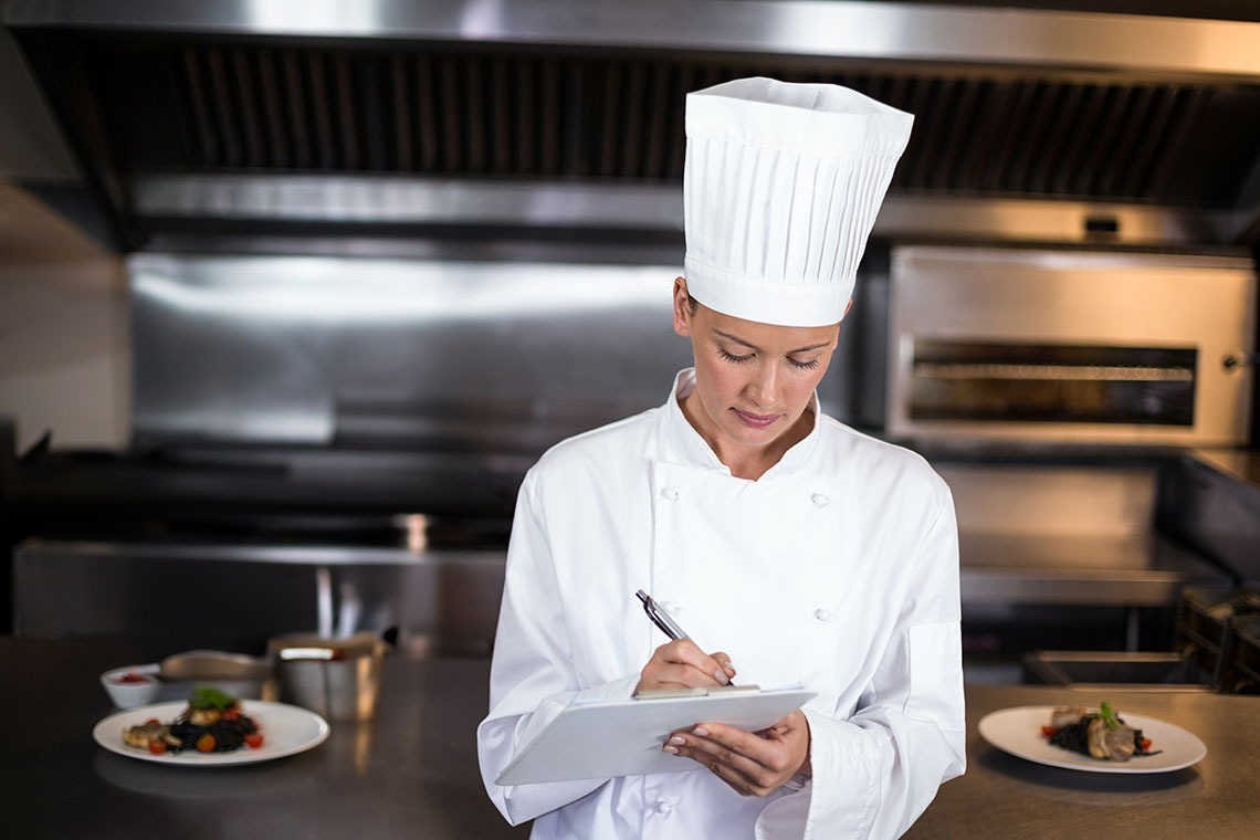 Alexandre Corporativa hotel chef reviewing notes in a modern kitchen with plated dishes.