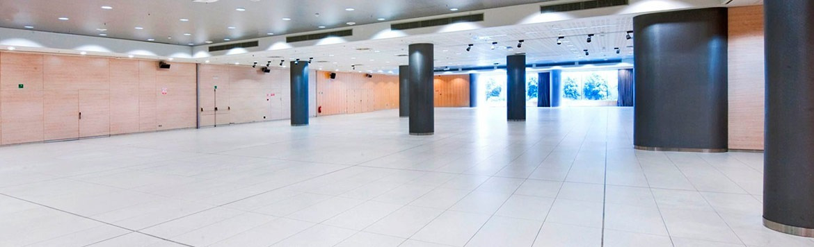 Grande salle de conférence moderne Alexandre Corporativa avec sol blanc, murs bois et piliers sombres.
