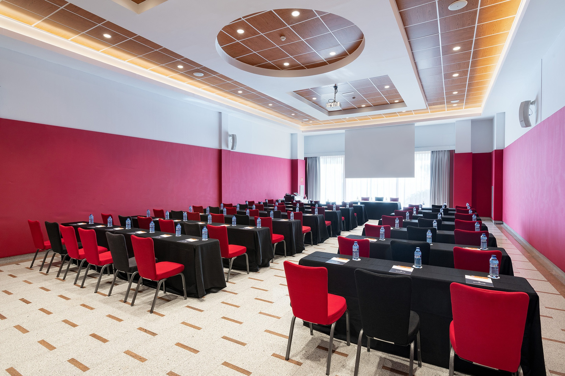 Sala de reuniones Alexandre Corporativa con mesas, sillas rojas y pantalla de proyector para eventos.