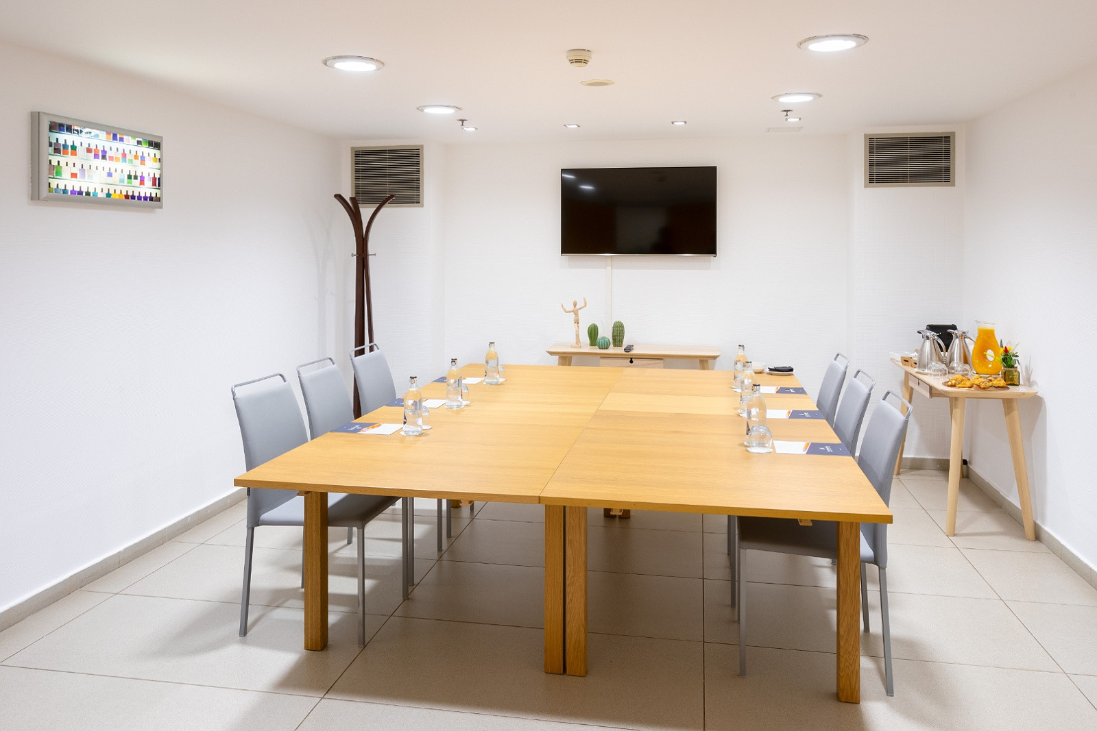 Salle de réunion Alexandre Corporativa avec table en bois, chaises grises et écran plat.