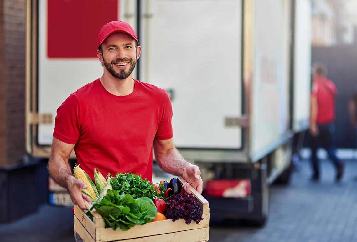 Smiling man in red delivers fresh produce crate for Alexandre Corporativa.