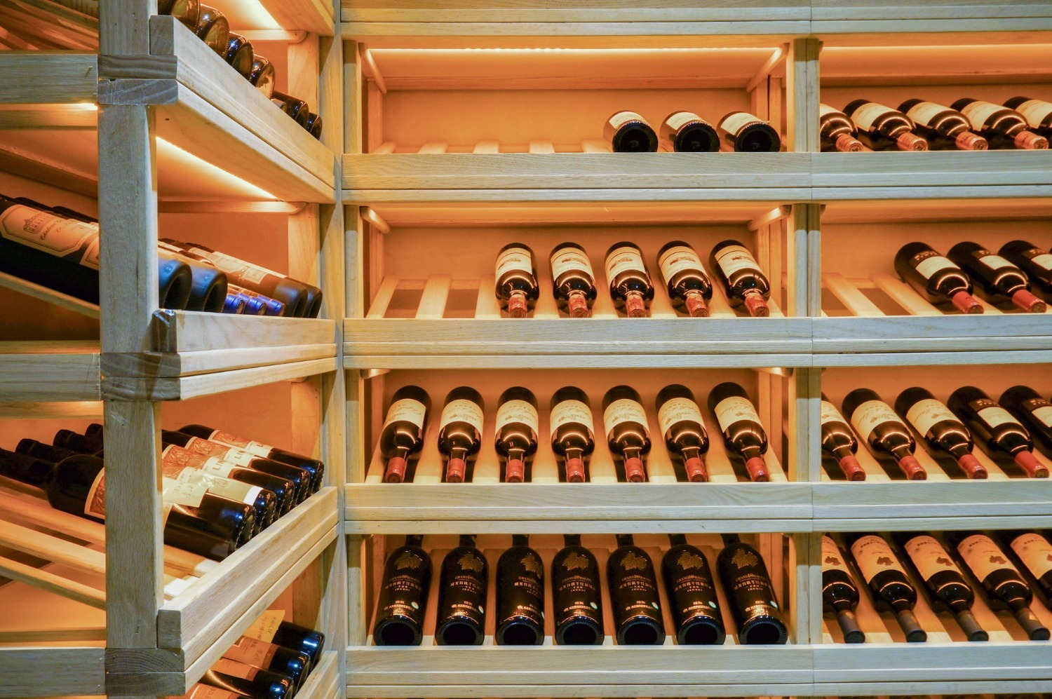 Bodega de vinos premium en el hotel Alexandre Corporativa, con estantes de madera iluminados y botellas de vino.