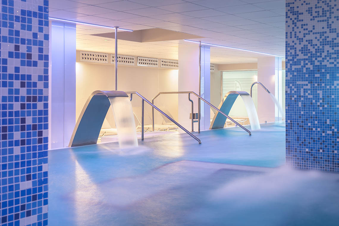 Piscina moderna con chorros de agua, mosaicos azules y arte vibrante en Hotel Alexandre Corporativa.
