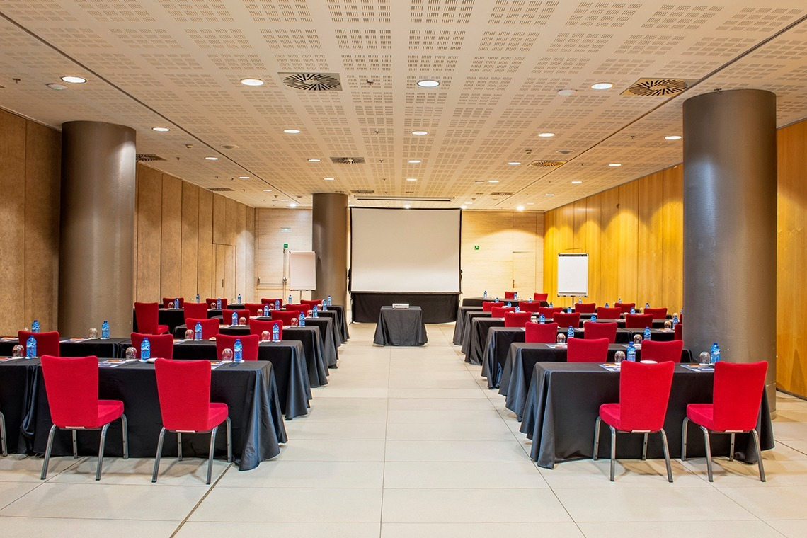 Salle de réunion moderne Alexandre Corporativa avec tables noires, chaises rouges et écran, idéale pour séminaires.
