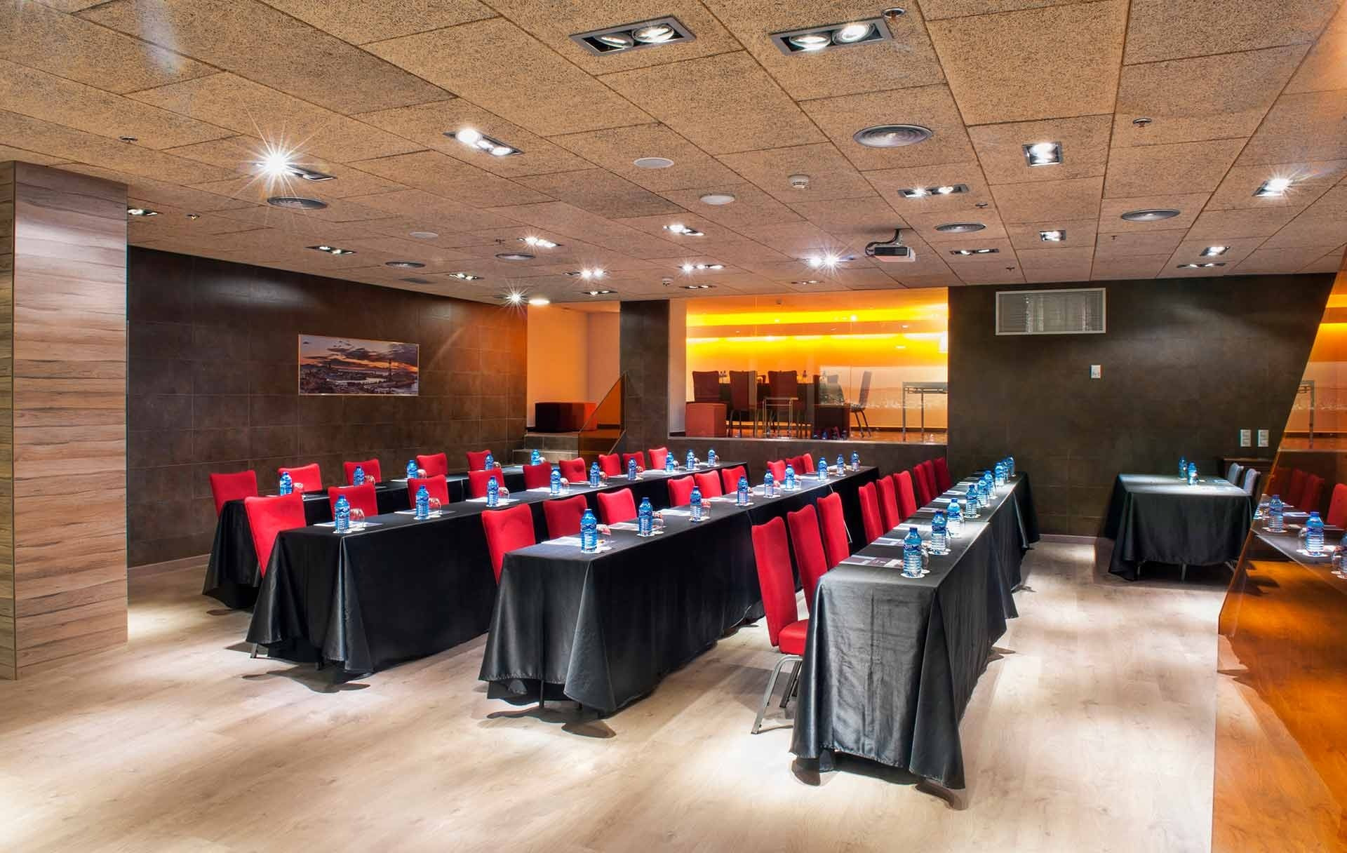 Alexandre Corporativa conference room with rows of red chairs, black tables, water bottles, and projector setup.