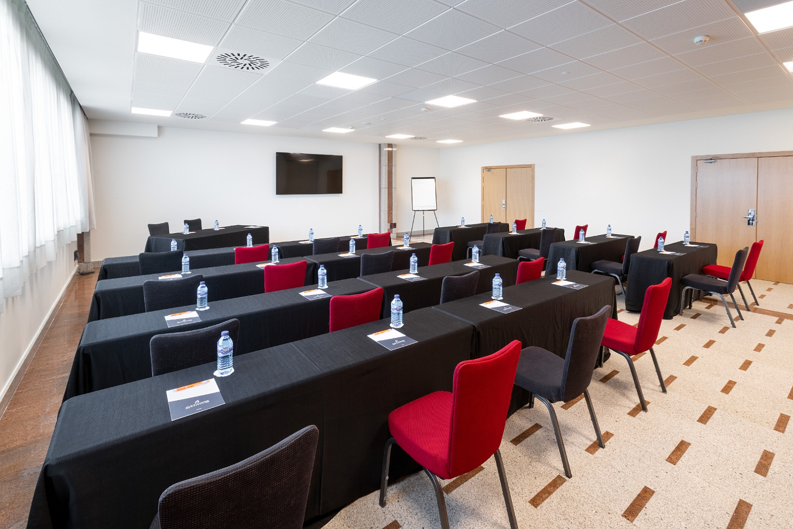Configuración de sala para eventos Alexandre Corporativa, con sillas rojas y negras y mesa para ponentes.