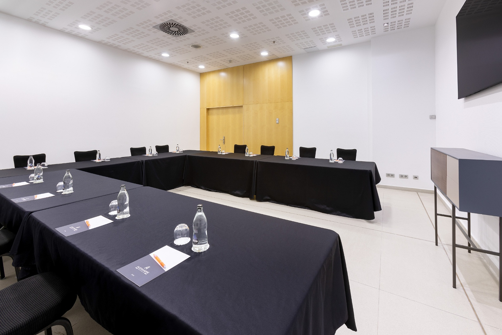 Salle de réunion Alexandre Corporativa avec tables noires, chaises et écran.