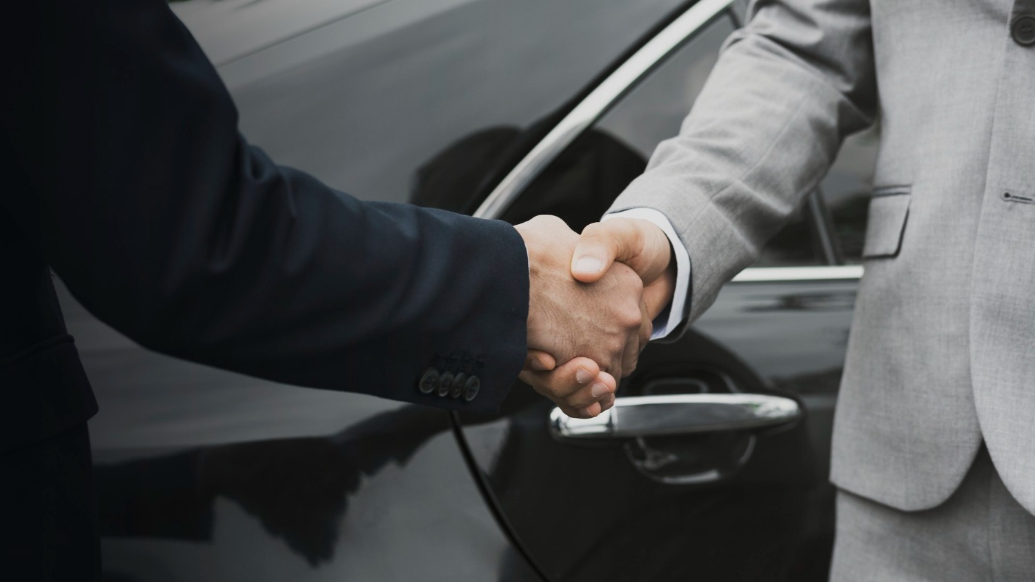 Dos empresarios se dan la mano frente a un coche, simbolizando acuerdos Alexandre Corporativa.