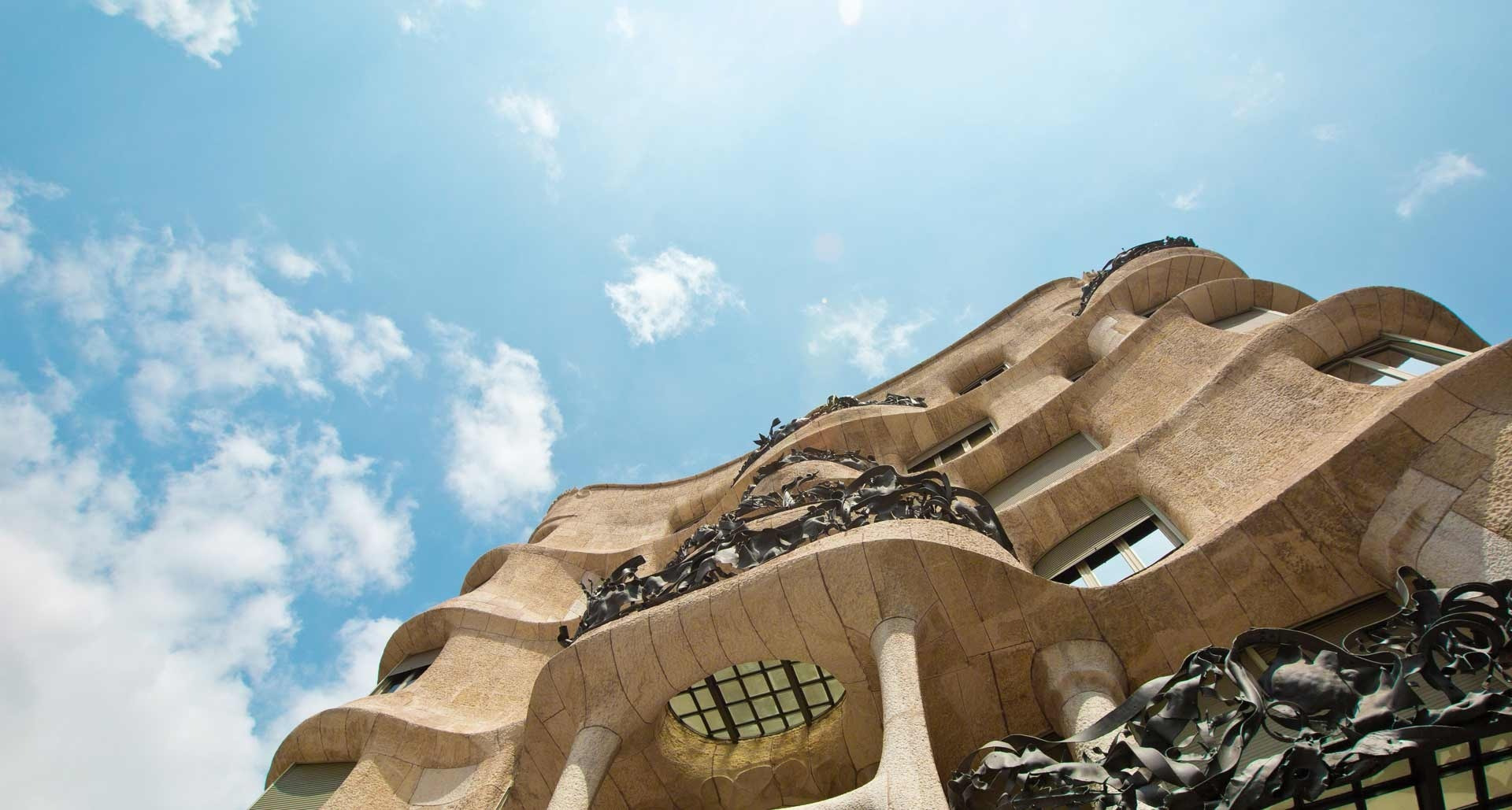 Wavy stone building facade with artistic iron balconies against blue sky, near Alexandre Corporativa hotels.