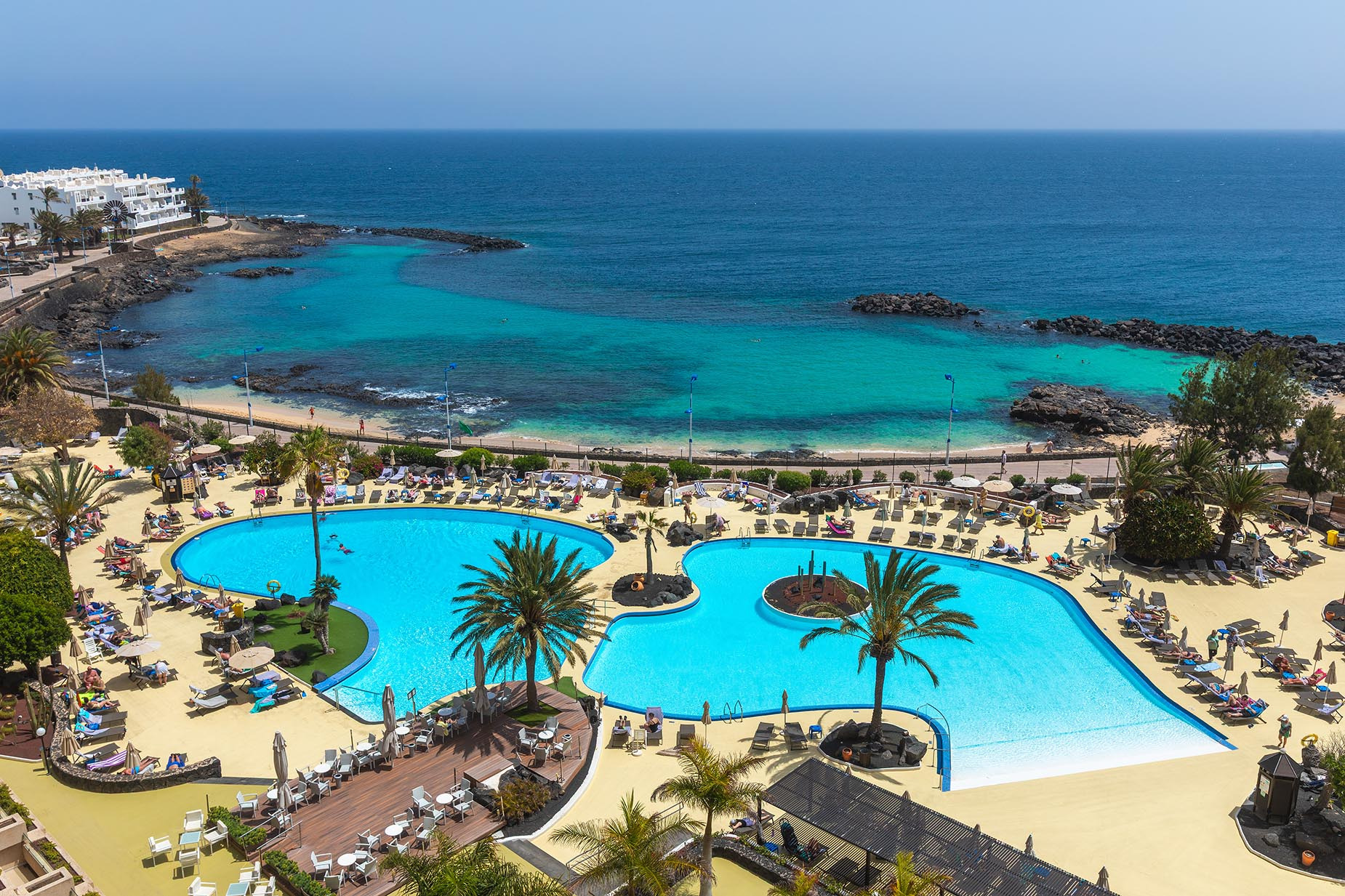 Luxuriöser Poolbereich eines Hotels am Meer mit Liegestühlen, Palmen und Blick auf den Ozean. Alexandre Teguise Playa | 4-Sterne-Hotel auf Lanzarote