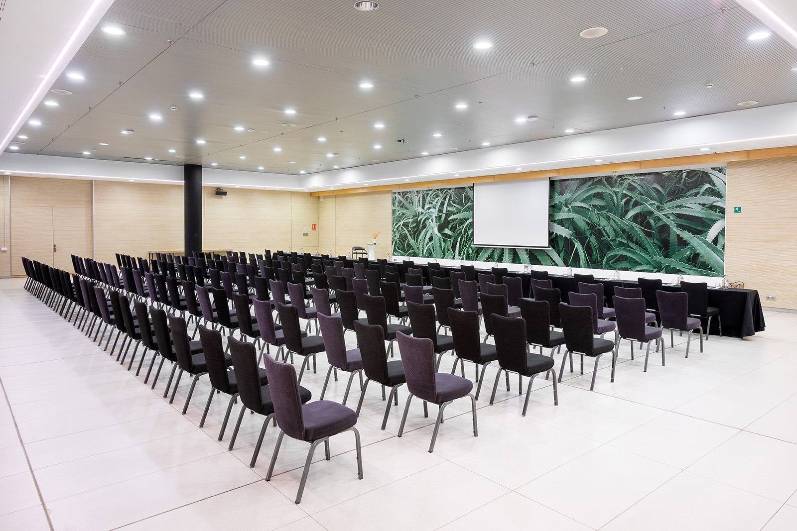 Salle de conférence Alexandre Corporativa prête pour événements, avec tables, écran, décor végétal.