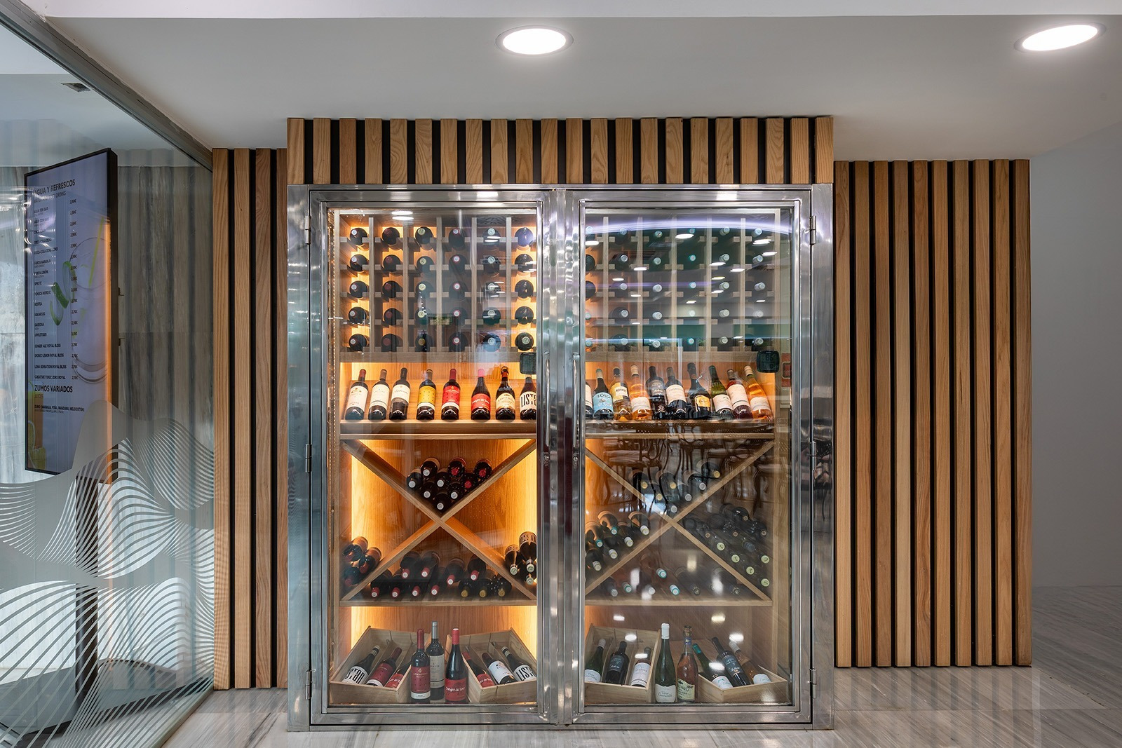Alexandre Corporativa's sleek wine cellar, illuminated, showcasing diverse wines within a modern wood design.