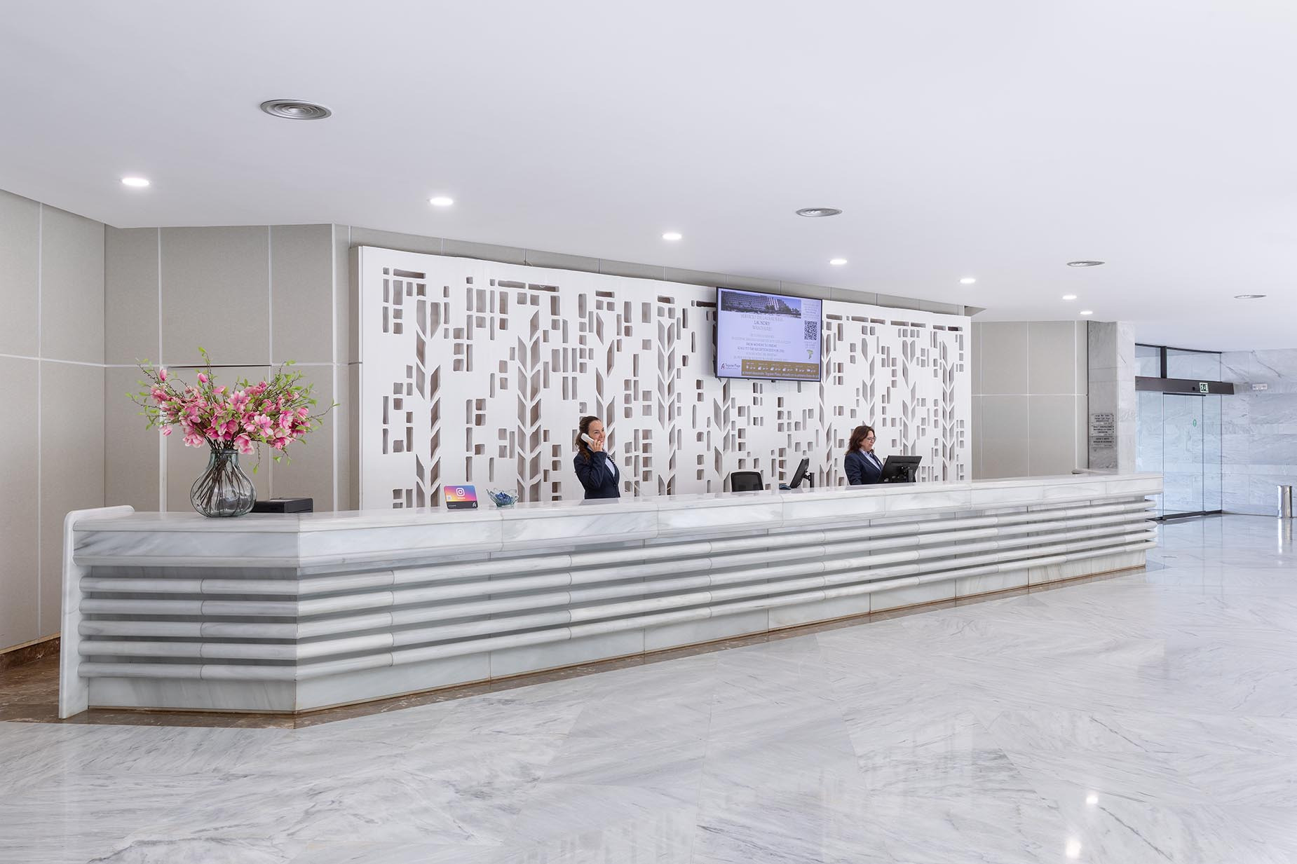 Helle Hotelrezeption mit lächelndem Personal und roten Absperrbändern. Modernes Design, willkommen für Alexandre Corporativa.