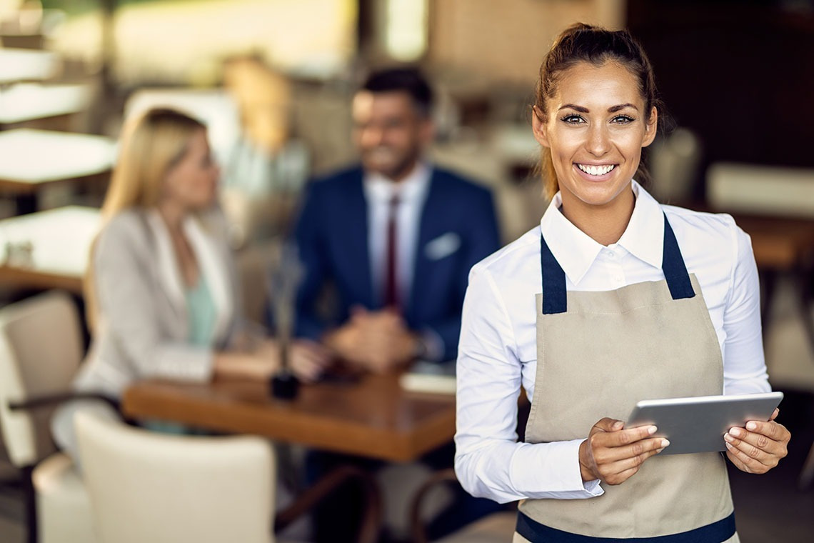 Smiling Alexandre Corporativa hotel server with tablet ready for guests.