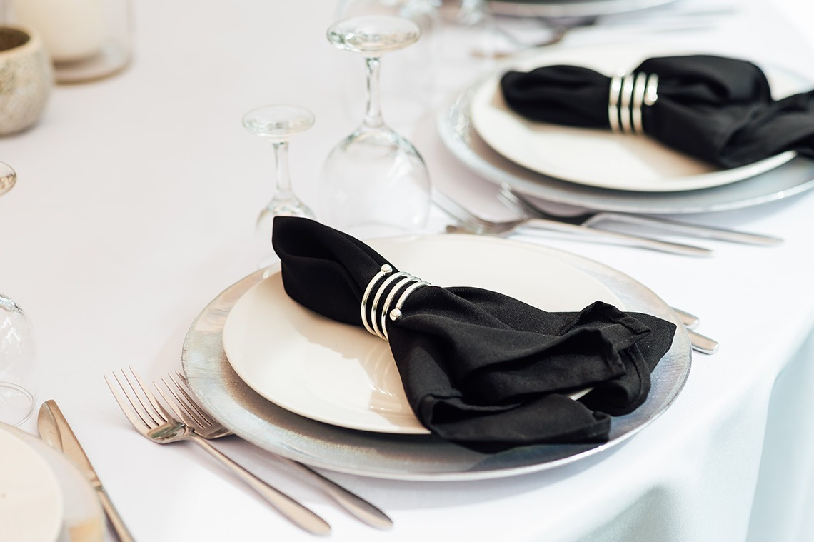 Configuración de mesa elegante para evento Alexandre Corporativa, con servilletas negras y detalles plateados.