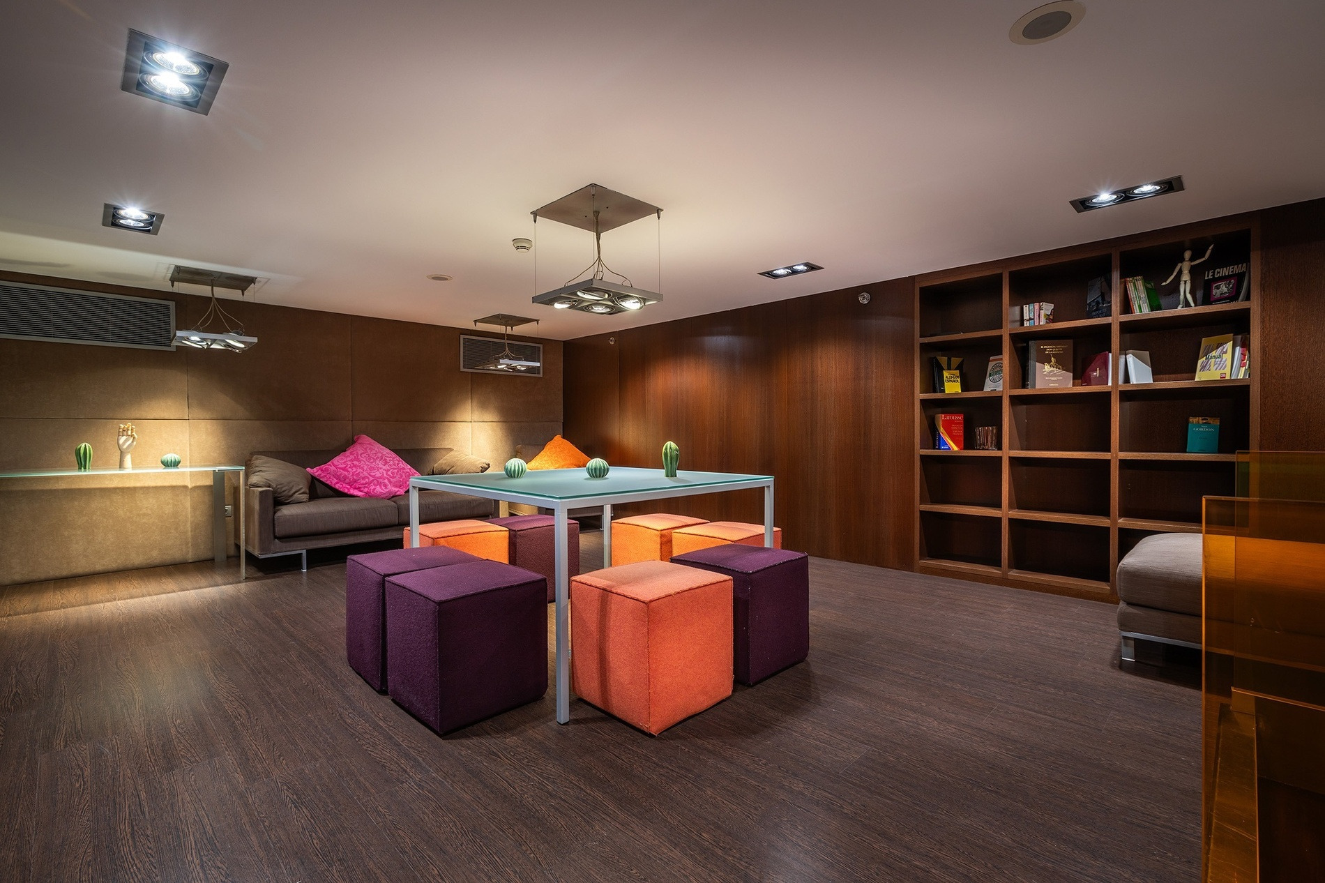 Salon moderne Alexandre Corporativa avec canapé, poufs colorés, bibliothèque et ambiance chaleureuse.