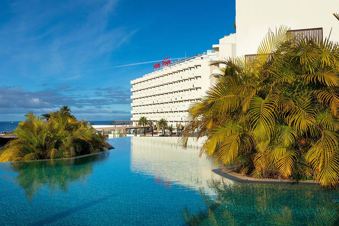 Hotel Alexandre Troya: Pool mit Palmen vor einem modernen Hotelgebäude am Meer