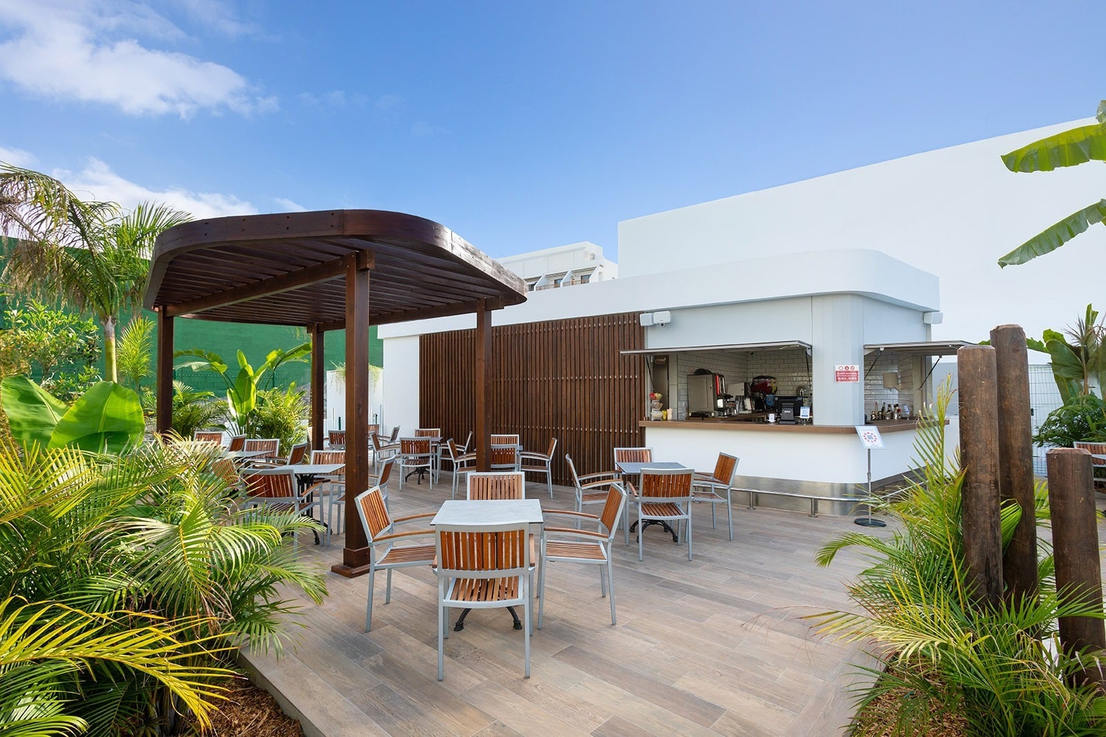 Alexandre Corporativa outdoor cafe with modern bar, wooden pergola, and lush tropical plants.