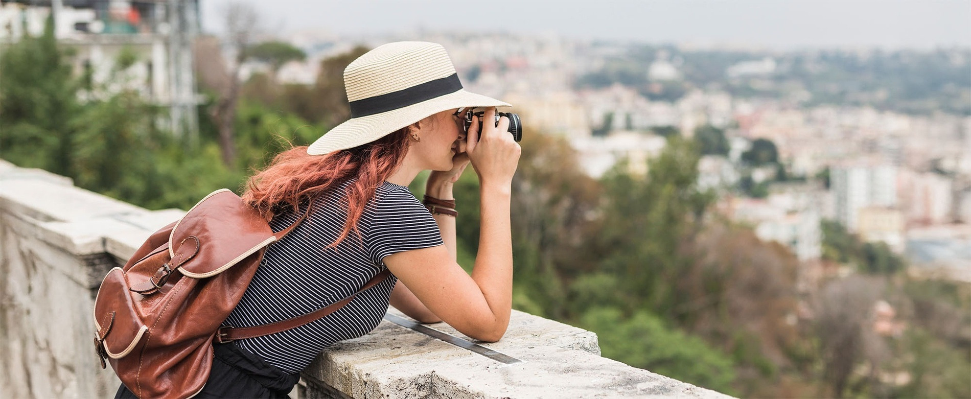 Woman photographer with hat & backpack capturing city panorama. Discover Alexandre Hotels offers and promotions.