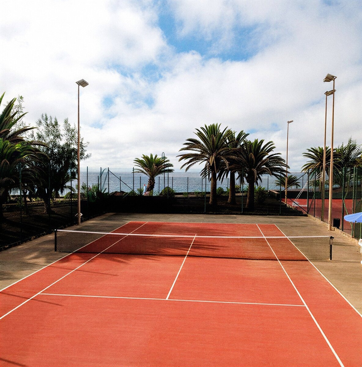 Pista de tenis roja al aire libre de Alexandre Corporativa con palmeras y vistas al mar.