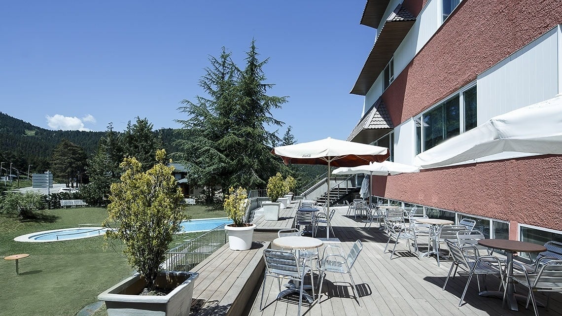 a deck with tables chairs and umbrellas with a pool in the background