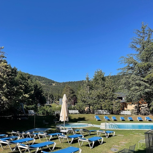 una piscina rodeada de tumbonas azules y una sombrilla blanca