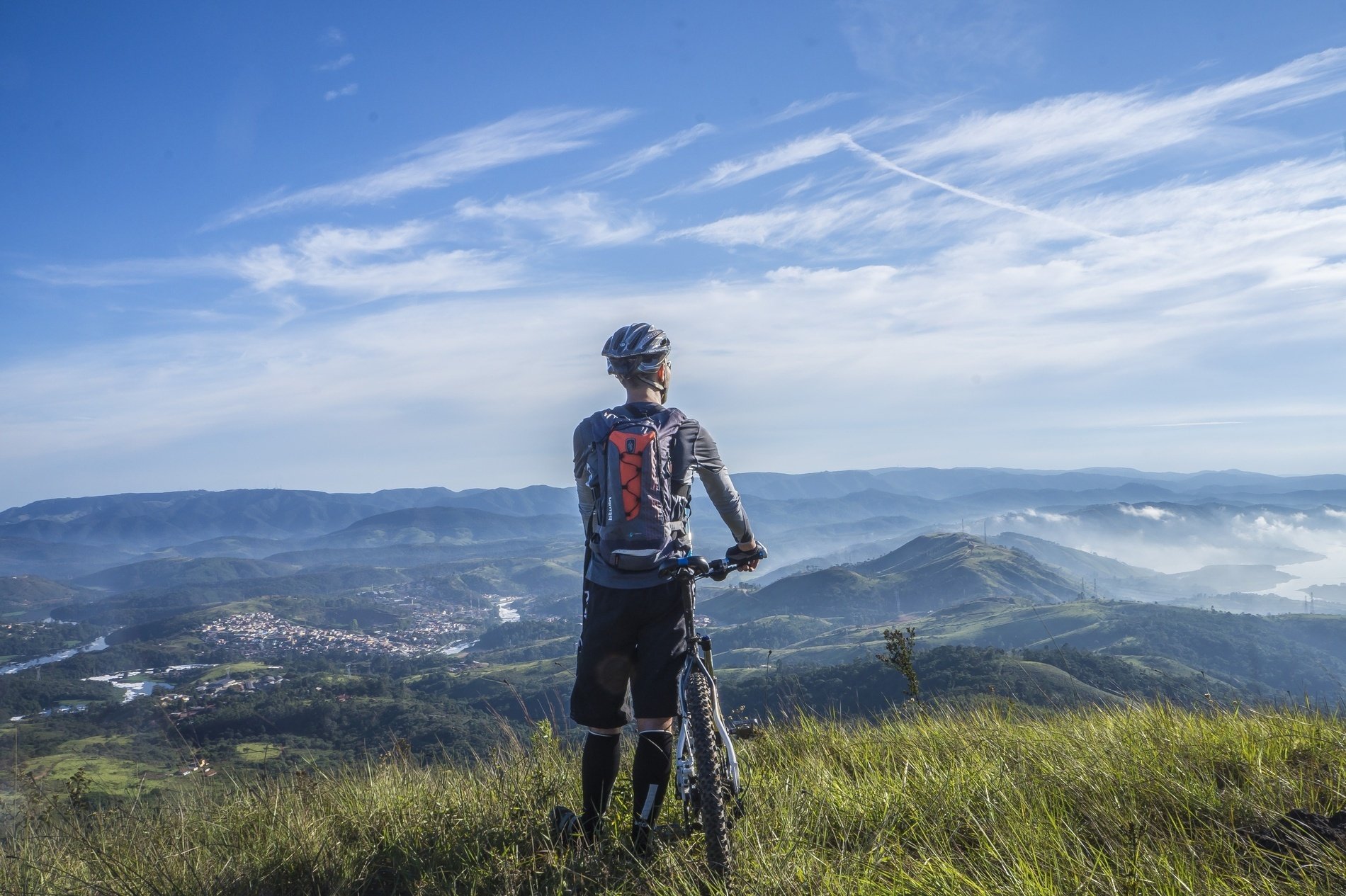 un hombre con una mochila roja sostiene una bicicleta en la cima de una colina