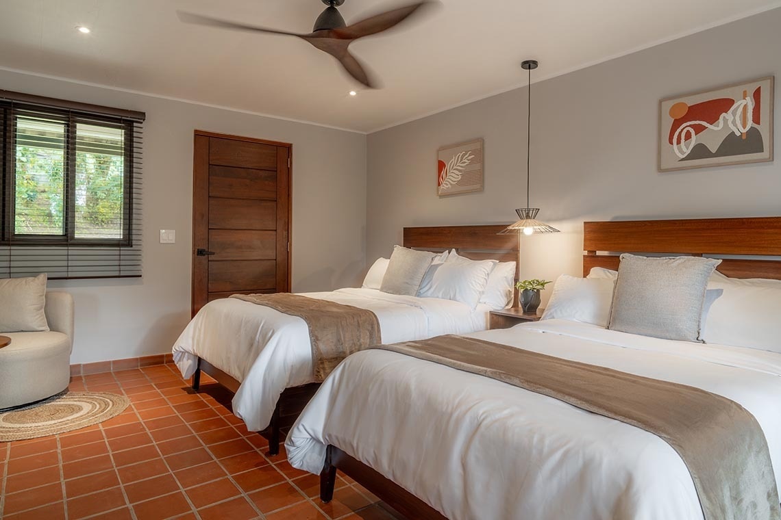 Dormitorio luminoso con dos camas, suelo de baldosas de terracota y decoración moderna.