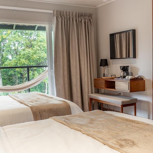 Una habitación luminosa con dos camas, un balcón con hamaca y vista a la exuberante vegetación, y una estación de café.