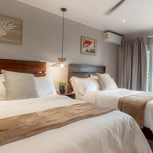 Dormitorio luminoso y moderno con dos camas, decoración en tonos neutros y un balcón con hamaca que ofrece vistas a la vegetación.