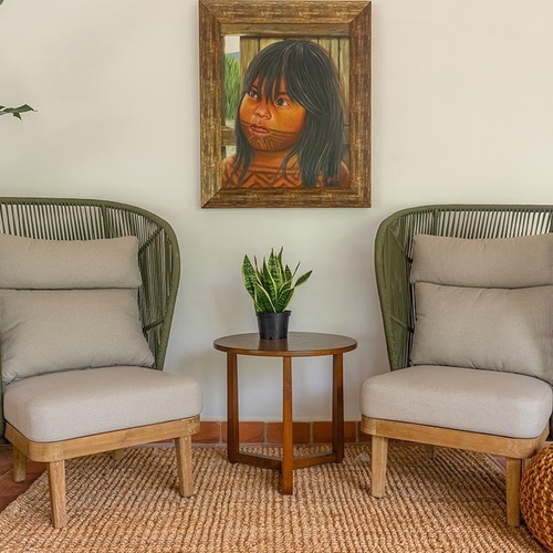 Dos cómodos sillones verdes con cojines beige, una mesa con una planta y un retrato de un niño decoran un espacio acogedor con alfombra de yute.