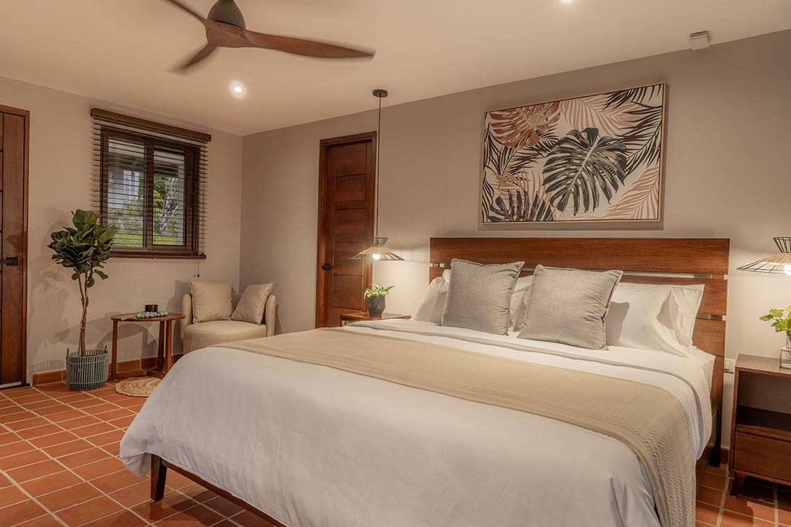 Un dormitorio moderno y acogedor con una cama grande, suelo de terracota, muebles de madera oscura y toques tropicales.