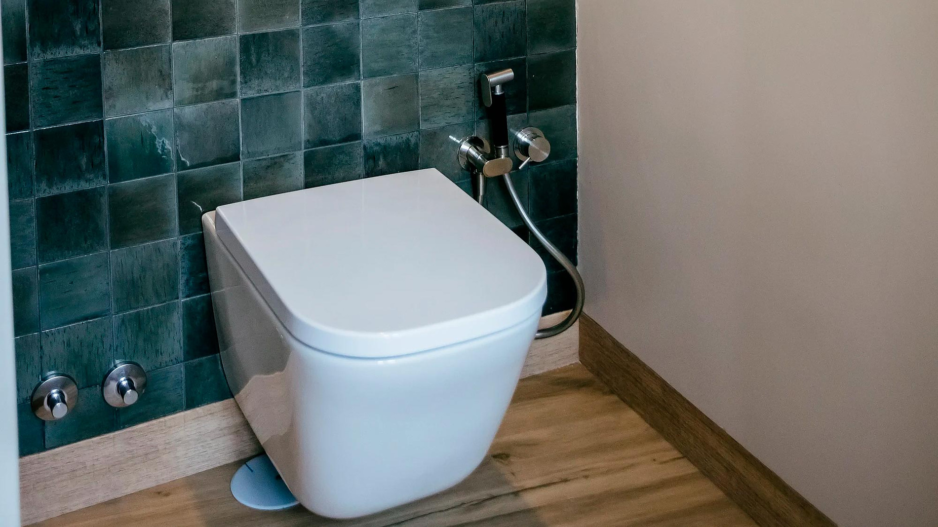 Banheiro moderno com azulejos verdes e vaso sanitário suspenso. Experiência AndTales.