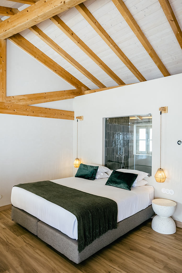 Cozy AndTales bedroom with exposed beams, plush green pillows, and modern pendant lights.