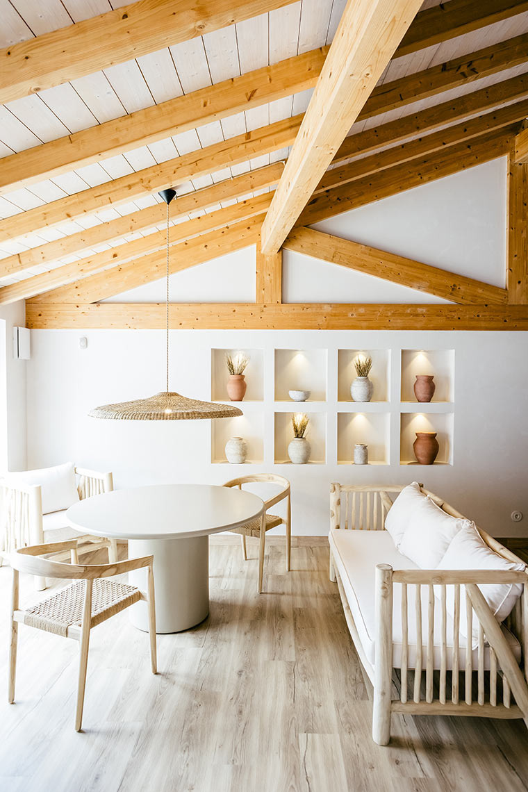 Elegant AndTales hotel dining area with white table, chairs, and natural wood beams.