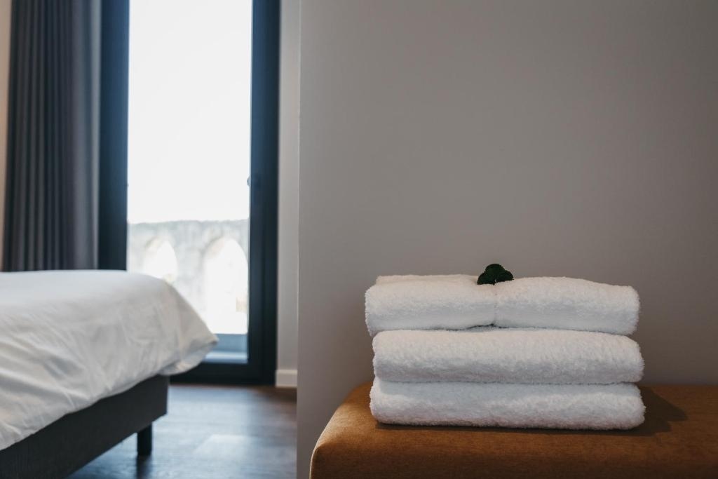 Fresh white towels AndTales on a plush seat near a large window and hotel bed.