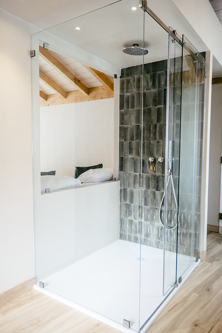 AndTales modern glass shower enclosure with tiled accent wall.