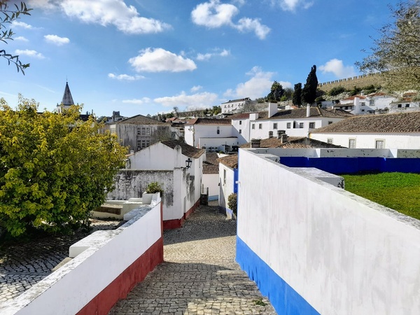AndTales: charmosa viela em Óbidos, Portugal, com casas caiadas e muro decorado.