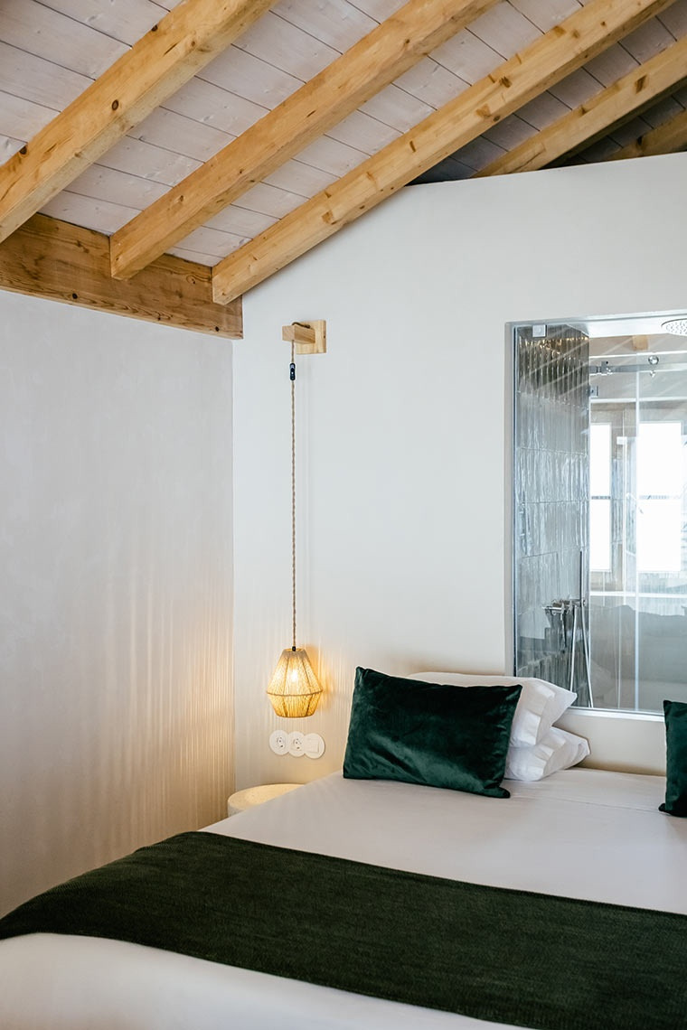 Cozy AndTales bedroom with exposed beams, a stylish pendant light, and a luxurious green velvet pillow.