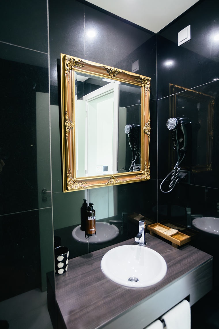 Espelho decorativo em banheiro de hotel AndTales com bancada, pia e secador de cabelo.