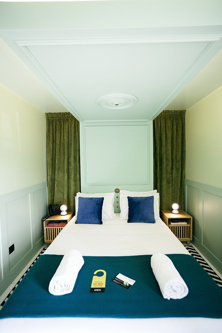 Quarto AndTales: cama com lençóis brancos, almofadas azuis, mantas e porta para não perturbar.