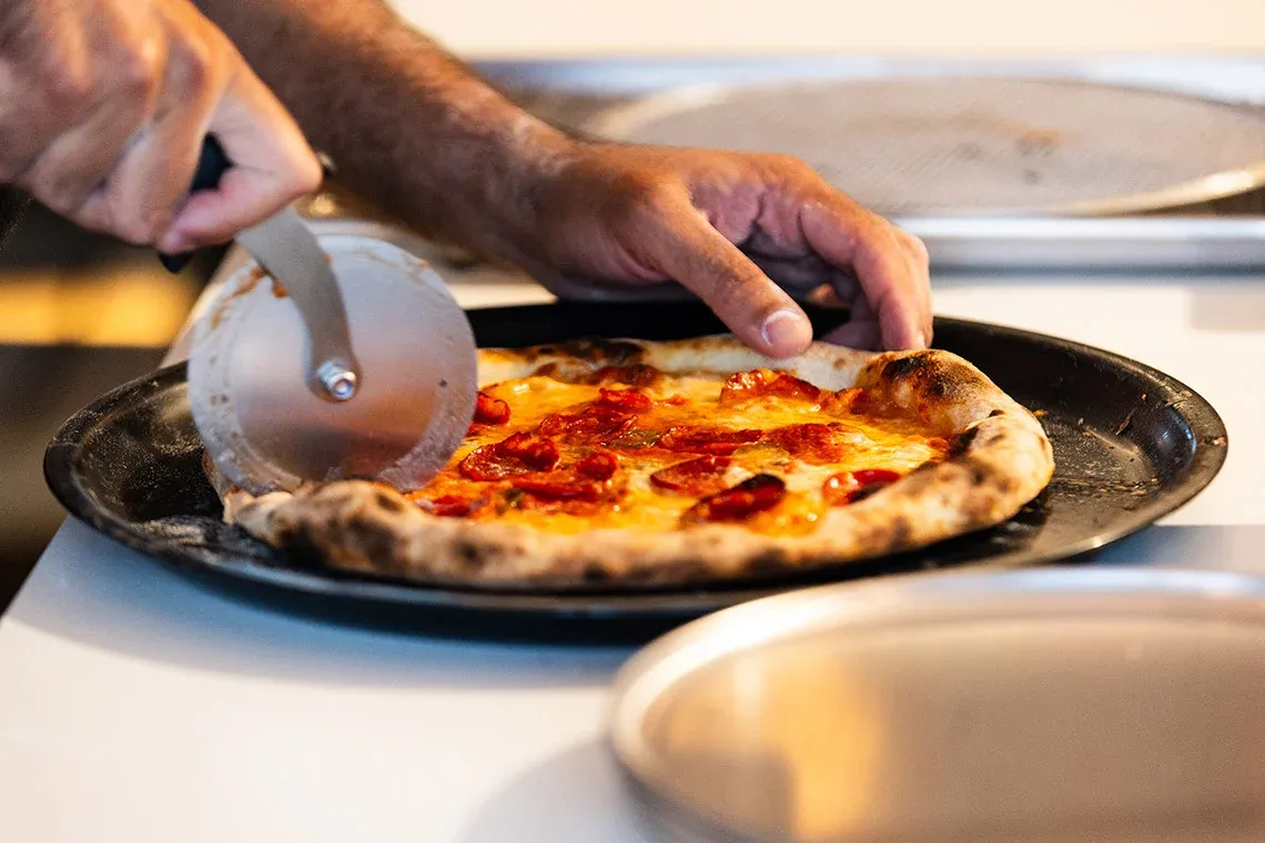 Pizza apetitosAndTales sendo cortada na cozinha de um hotel.